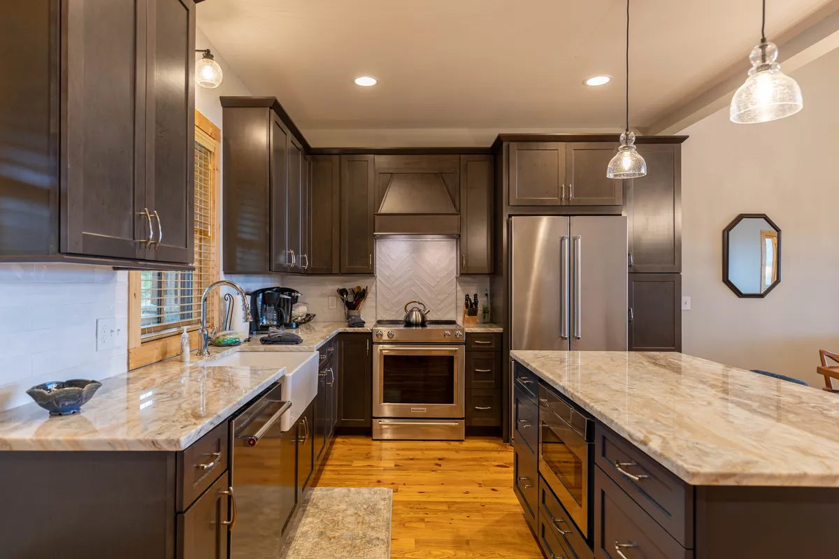 This image showcases a modern kitchen with granite countertops, stainless steel appliances, wooden cabinetry, and stylish pendant lighting. The scene captures an inviting, airy atmosphere perfect for cooking and entertaining, with ample surfaces and the promise of communal activity.
