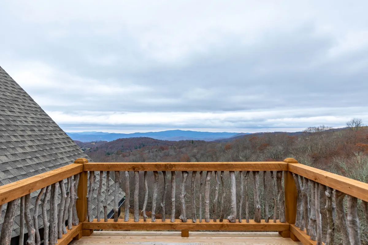 A serene view from the deck, highlighting a sturdy wooden railing and showcasing sweeping mountain vistas beneath a tranquil, cloudy sky. The space invites relaxation and contemplation, immersed in natural beauty.