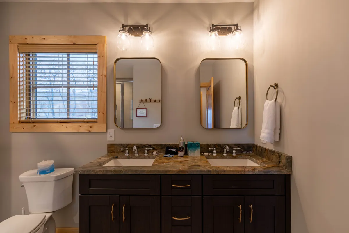 A stylish shared bathroom with a double sink vanity, large mirrors, and soft lighting. Wooden window frames add warmth, and the layout is perfect for accommodating multiple guests or family members.