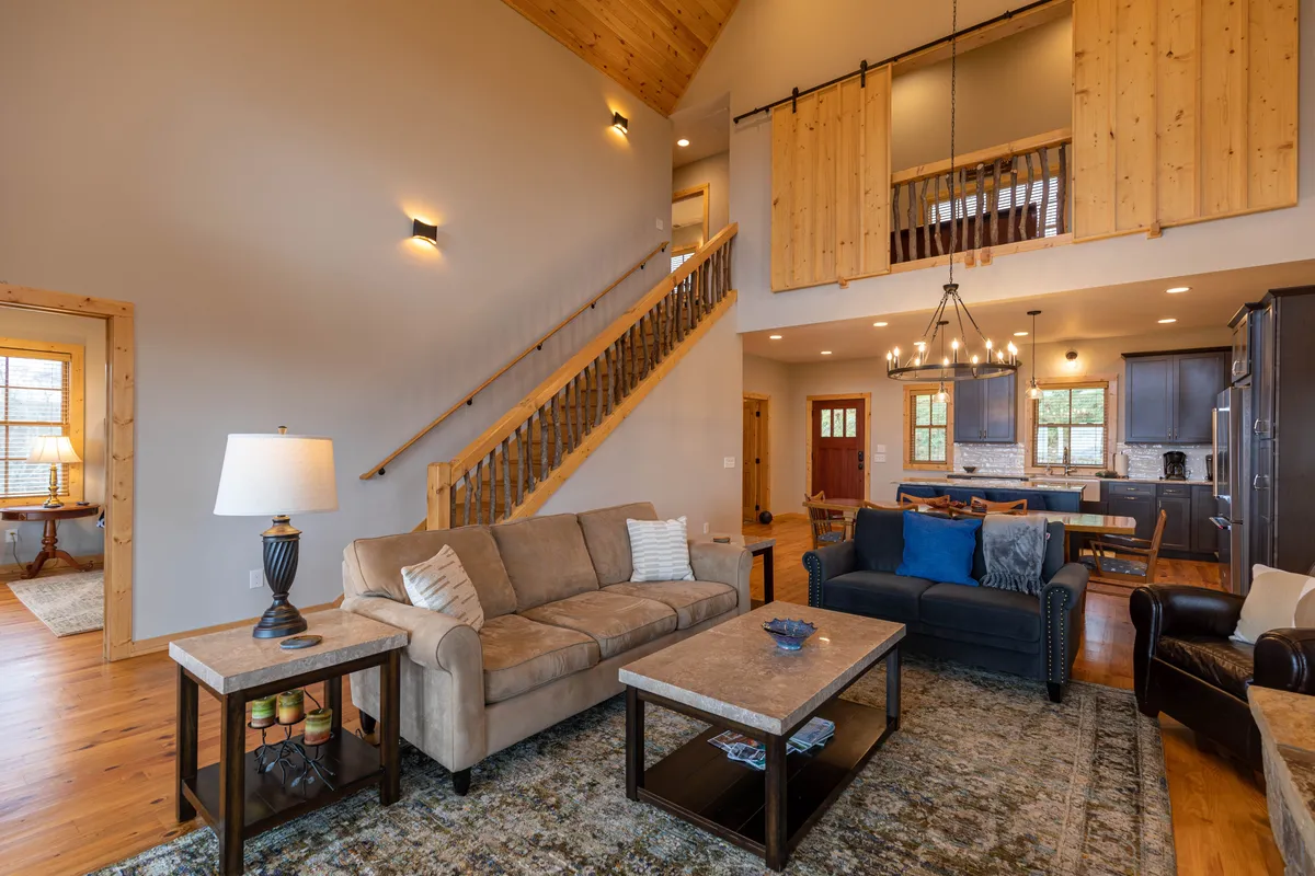 This image highlights the open-concept great room, featuring a comfortable sofa, coffee table, and a stylish chandelier beneath a staircase. The space is inviting, ideal for relaxing, socializing, and group activities like movie or game nights.