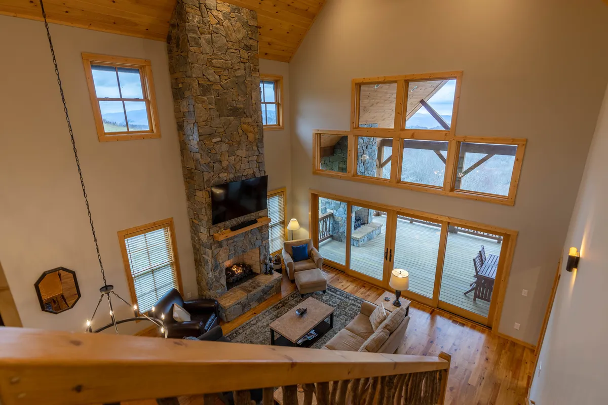 This shot focuses on the seating area centered around the stone fireplace, with a comfortable rug and large windows framing scenic views. The room feels cozy and intimate, ideal for relaxing, entertaining, or enjoying quiet moments by the fire.