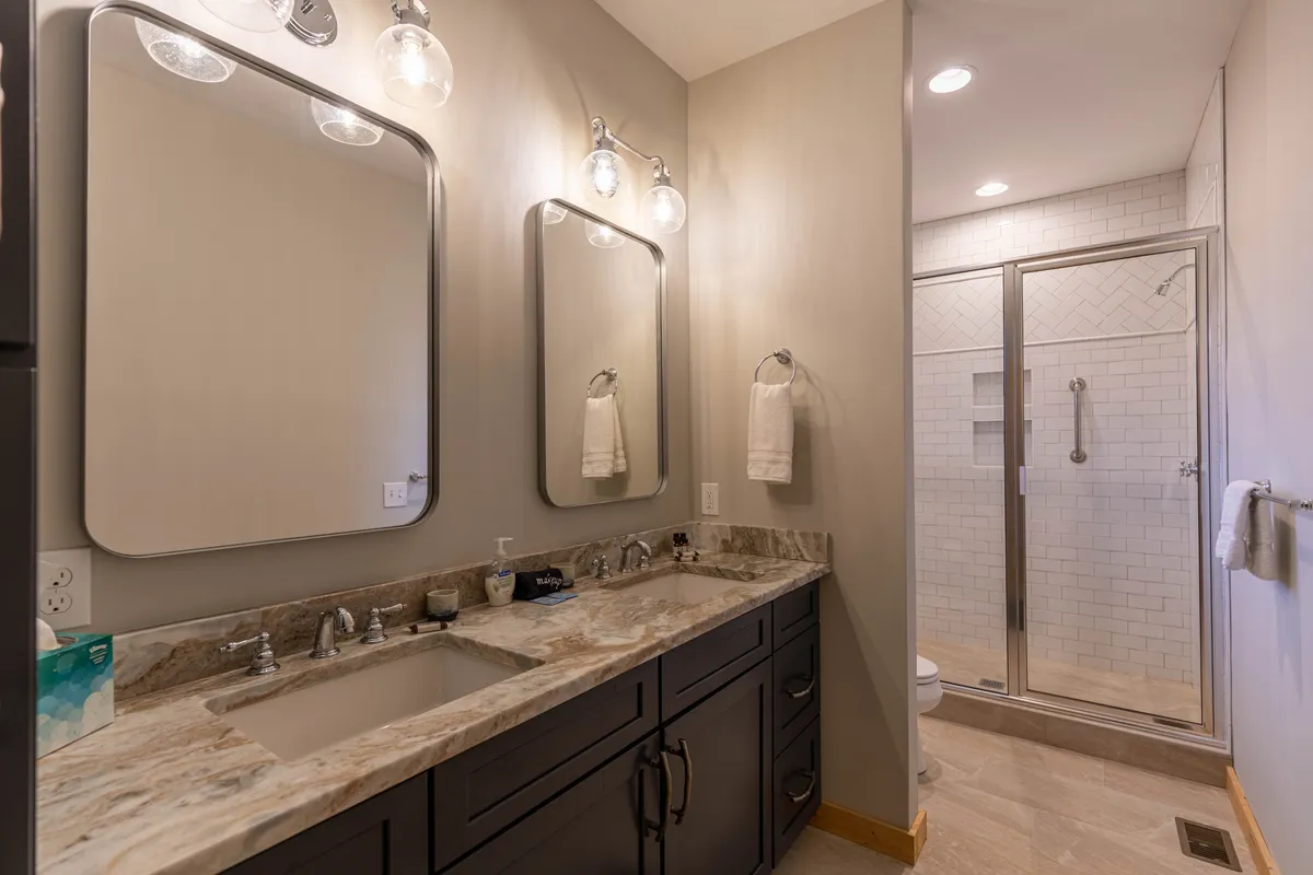 A bright, spa-inspired bathroom with a double marble vanity, mirrors above each sink, and a spacious glass shower enclosure. Morning light fills the space, creating a sense of luxury and relaxation.