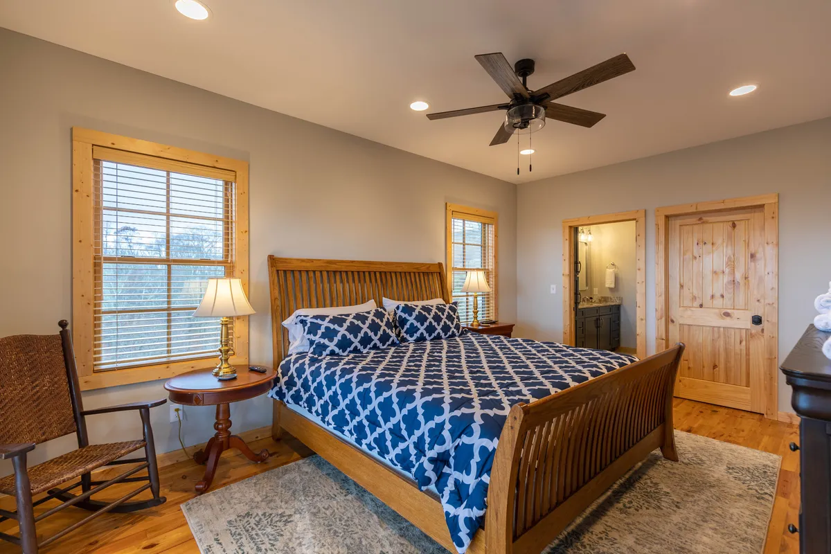 A welcoming bedroom with a large bed adorned in patterned bedding, a wooden rocking chair beside a window, a nightstand with a lamp, and sunlight gently streaming in. The space feels personal and restful, ideal for unwinding after a day of adventure.