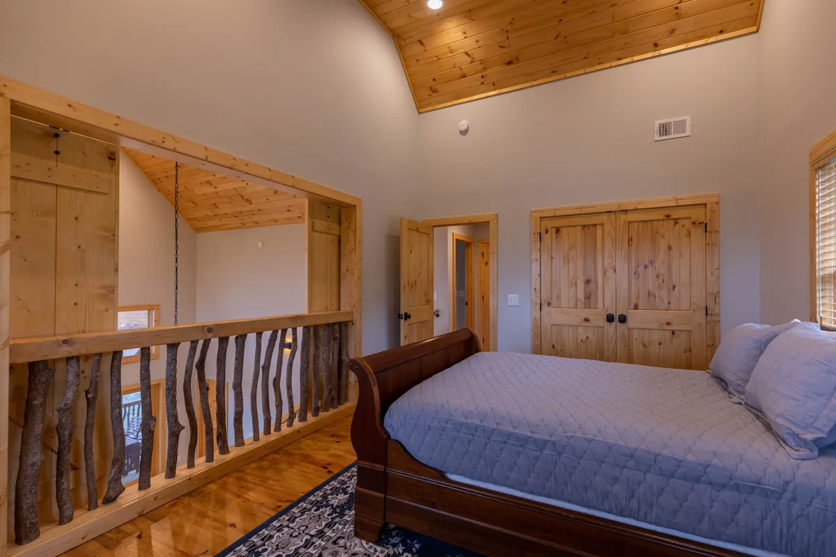 This tranquil bedroom features a wooden bed, textured accent wall, and natural wood railing, bathed in natural light. The serene ambiance invites restful nights and quiet mornings, supporting group comfort and privacy.