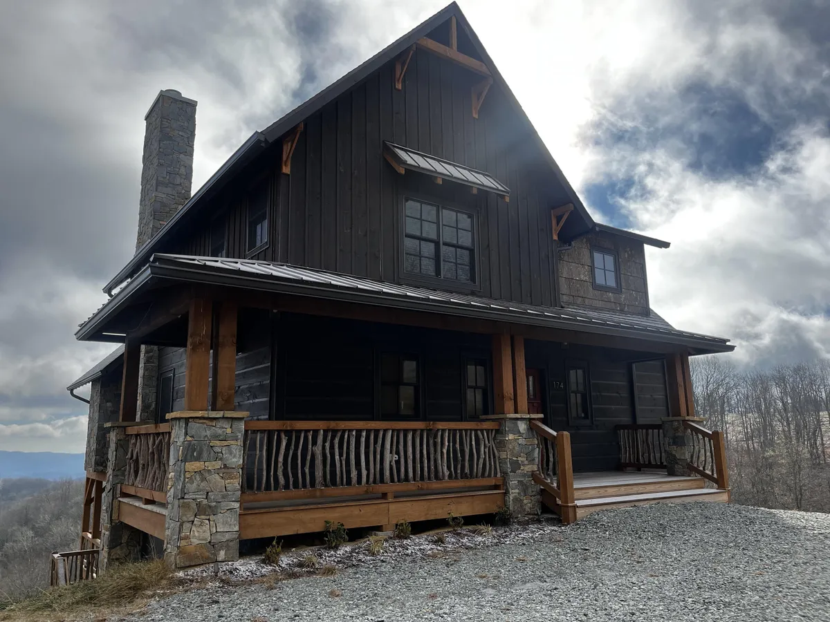 A cozy exterior view highlighting the stone chimney, wooden porch railing, and expansive front windows. The scene is inviting and suggests space for family gatherings or relaxing after a day of adventure.